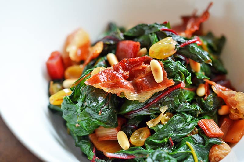 Swiss Chard salad with Raisins, Pine Nuts, and Porkitos in a bowl.