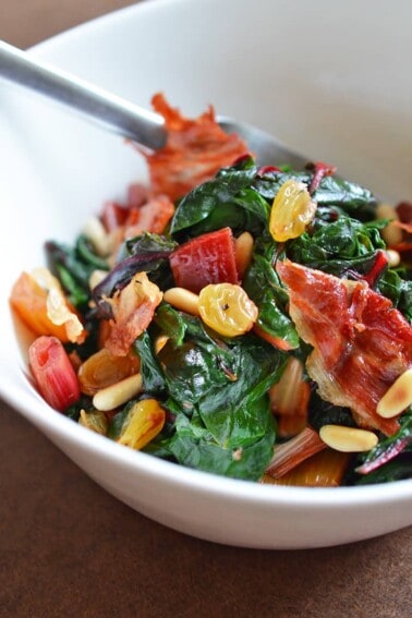 A white bowl filled with Swiss Chard with Raisins, Pine Nuts, and Porkitos