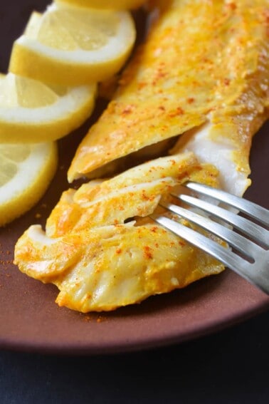 A closeup of perfectly cooked Tandoori Fish on a plate with sliced lemons.