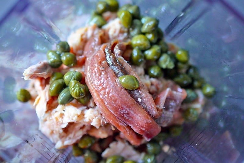 An overhead shot of the inside of a blender filled with ingredients for Tonnato Sauce before it has been blended.