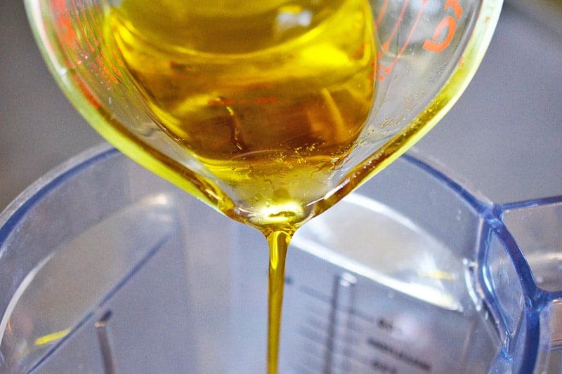 Pouring olive oil from a liquid measuring cup into an open blender container to make Tonnato Sauce 