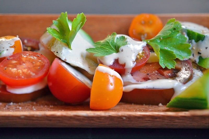 A closeup shot of a sliced tomato salad topped with creamy, Whole30 Tonnato Sauce and Italian parsley.