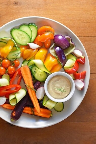 An overhead shot of a white plate filled with colorful raw vegetables and a small white ramekin filled with tonnato sauce.