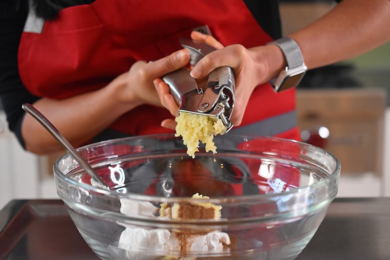 Someone adding minced garlic to a bowl.