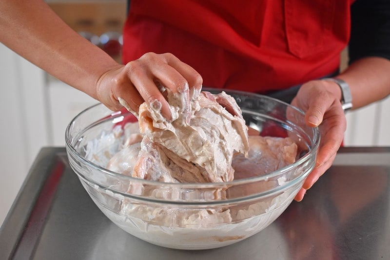 Someone using their hands to combine the chicken thighs and marinade for Umami Roast Chicken 