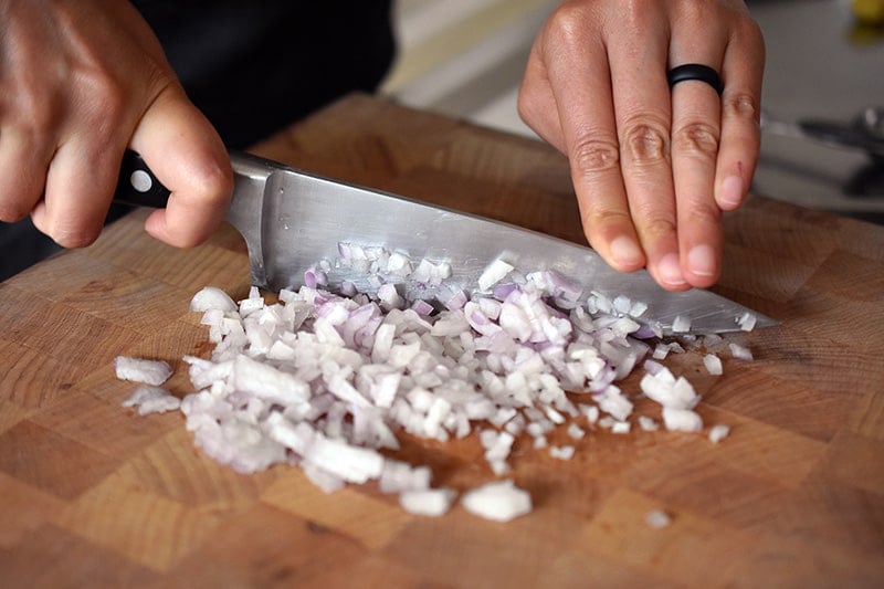 Mincing shallots on a wooden cutting board to make Vietnamese Lemongrass Chicken 