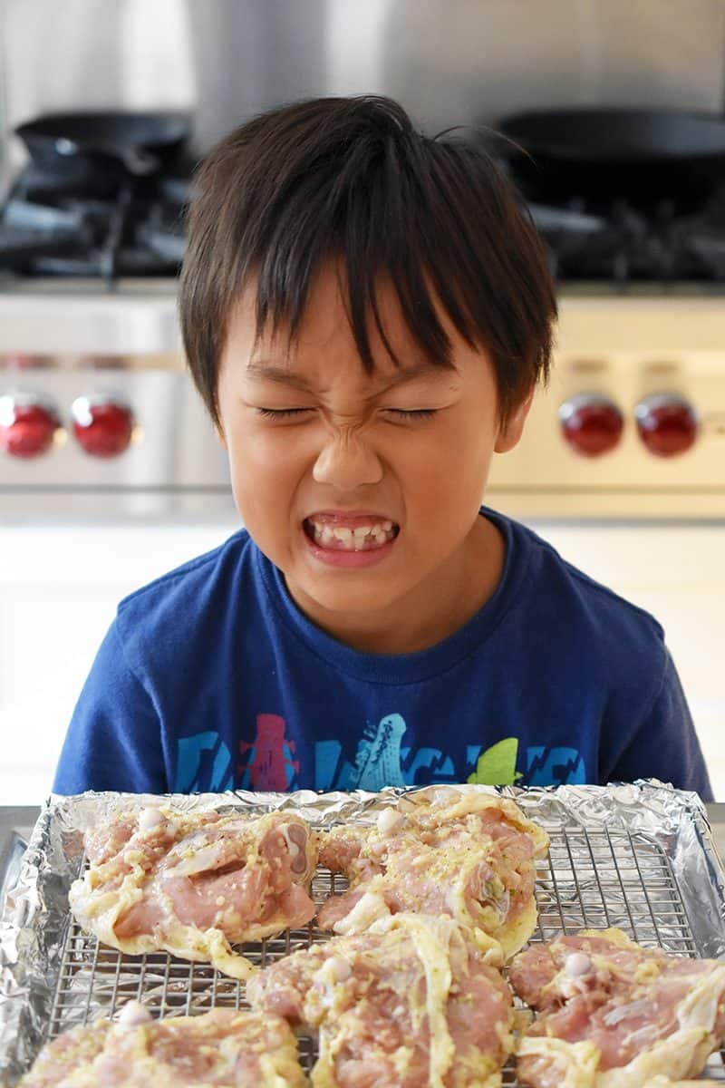 A cute kid making a funny face in front of a tray of Vietnamese Lemongrass Chicken 