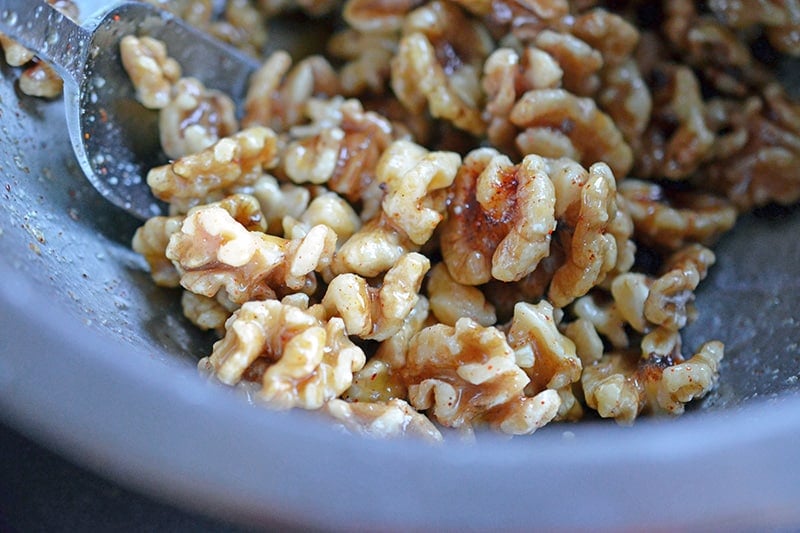 Tossing maple spiced walnuts in a bowl for gluten-free Paleo Walnut Shrimp 