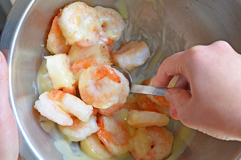 Tossing the Paleo Walnut Shrimp in the dressing in a silver bowl.