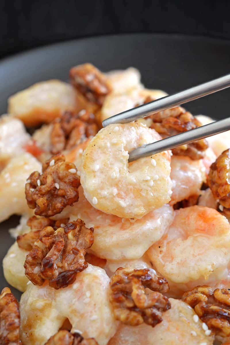 A pair of silver chopsticks picking up Paleo Walnut Shrimp on a black plate.