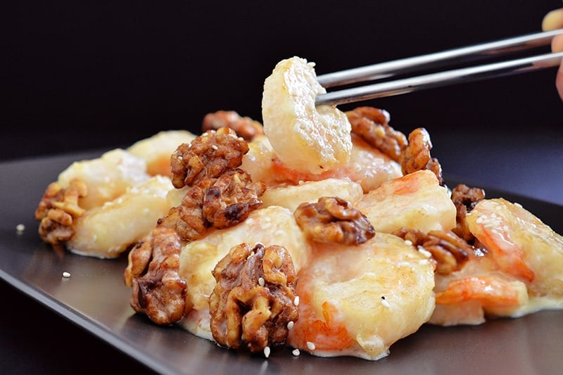 A side view of someone grabbing a piece of Paleo Walnut Shrimp with metal chopsticks