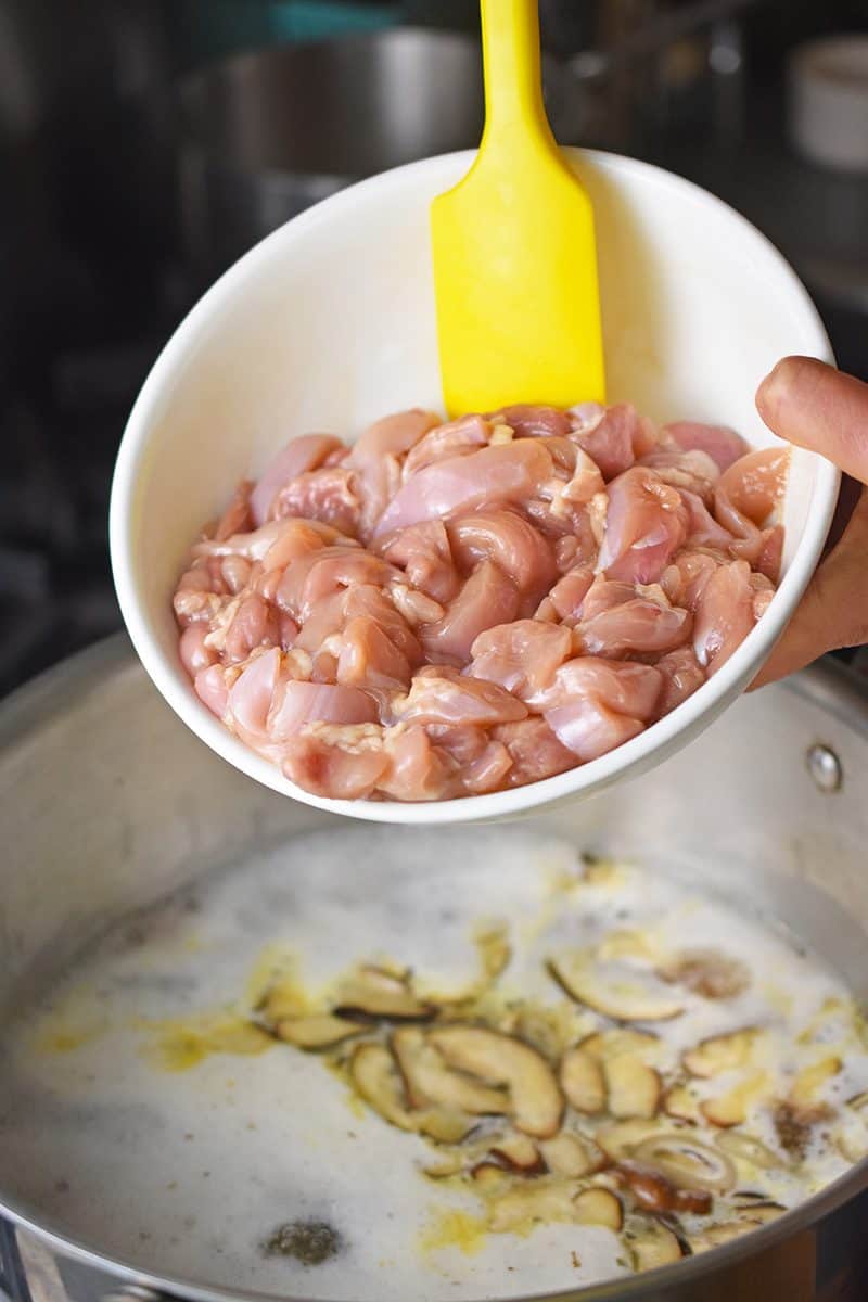 A bowl of marinated sliced chicken thighs is added to a pot of Watercress & Chicken Soup.
