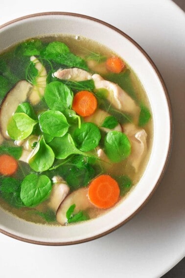 A ladle pouring Watercress & Chicken Soup into a serving bowl.