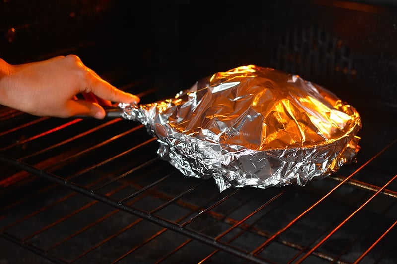 The foil-covered cast iron skillet with the seasoned cauliflower head is placed in the oven.