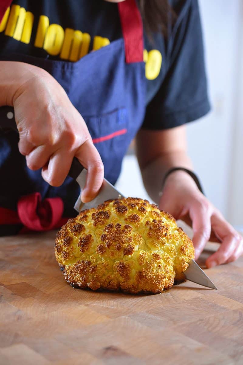Whole Roasted Cauliflower is sliced with a chef's knife.