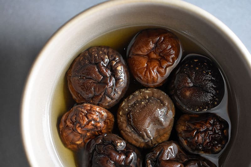 An overhead shot of a bowl of dried shiitake mushrooms soaked in water
