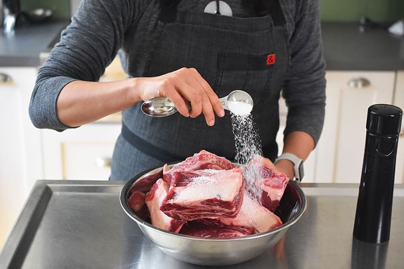 Salting short ribs in a metal bowl for Instant Pot Korean Short Ribs