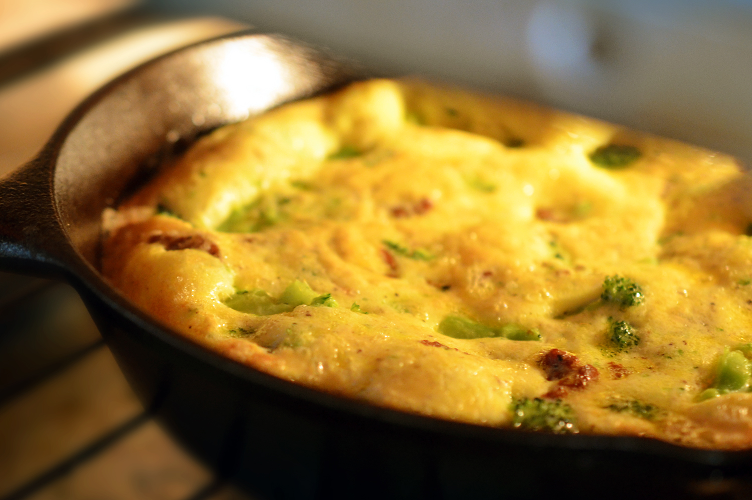 Close up of Easy Paleo Frittata baking in a toaster oven. The eggs are fully cooked and puffy yellow, with golden-brown edges.