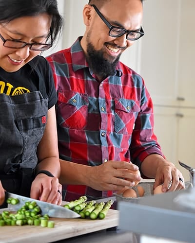 A smiling Asian woman and man are cooking together in a kitchen.