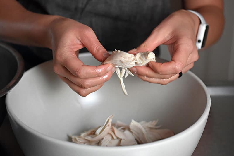 Shredding the chicken for Instant Pot Chicken Pho in a large bowl
