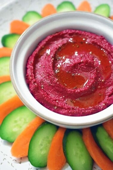 An overhead shot of paleo, Whole30, and vegan beet hummus in a white bowl surrounded by carrot and cucumber slices.