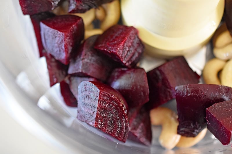 A close up of the beets and soaked cashews in a food processor.