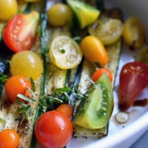 A deep white dish filled with broiled zucchini and roasted tomatoes.