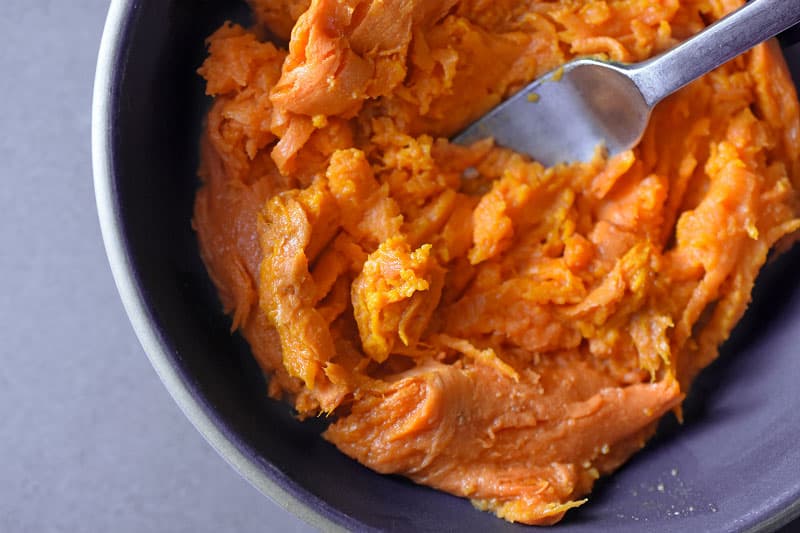 A bowl of cooked and mashed sweet potatoes with a fork in the bowl.