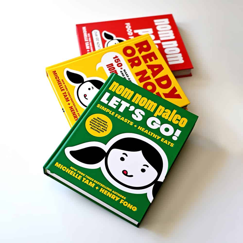 Three Nom Nom Paleo cookbooks splayed out on a white surface