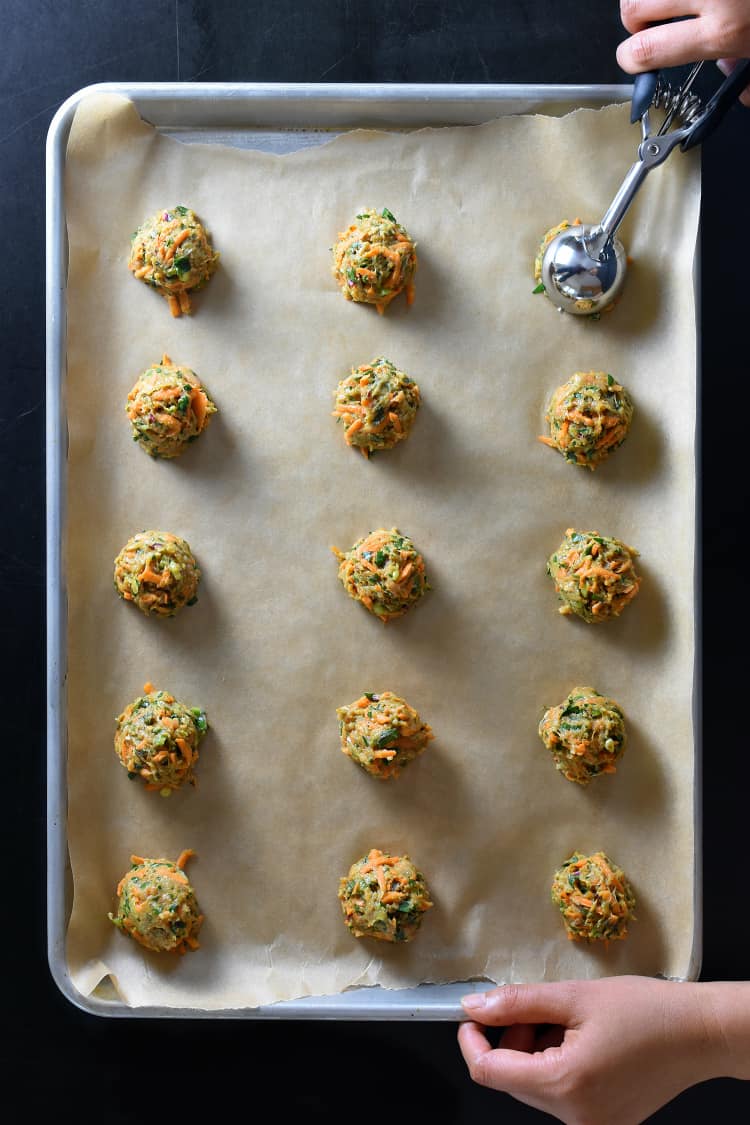 Using a scooper to portion out Curry Turkey Bites on a parchment lined rimmed baking sheet.