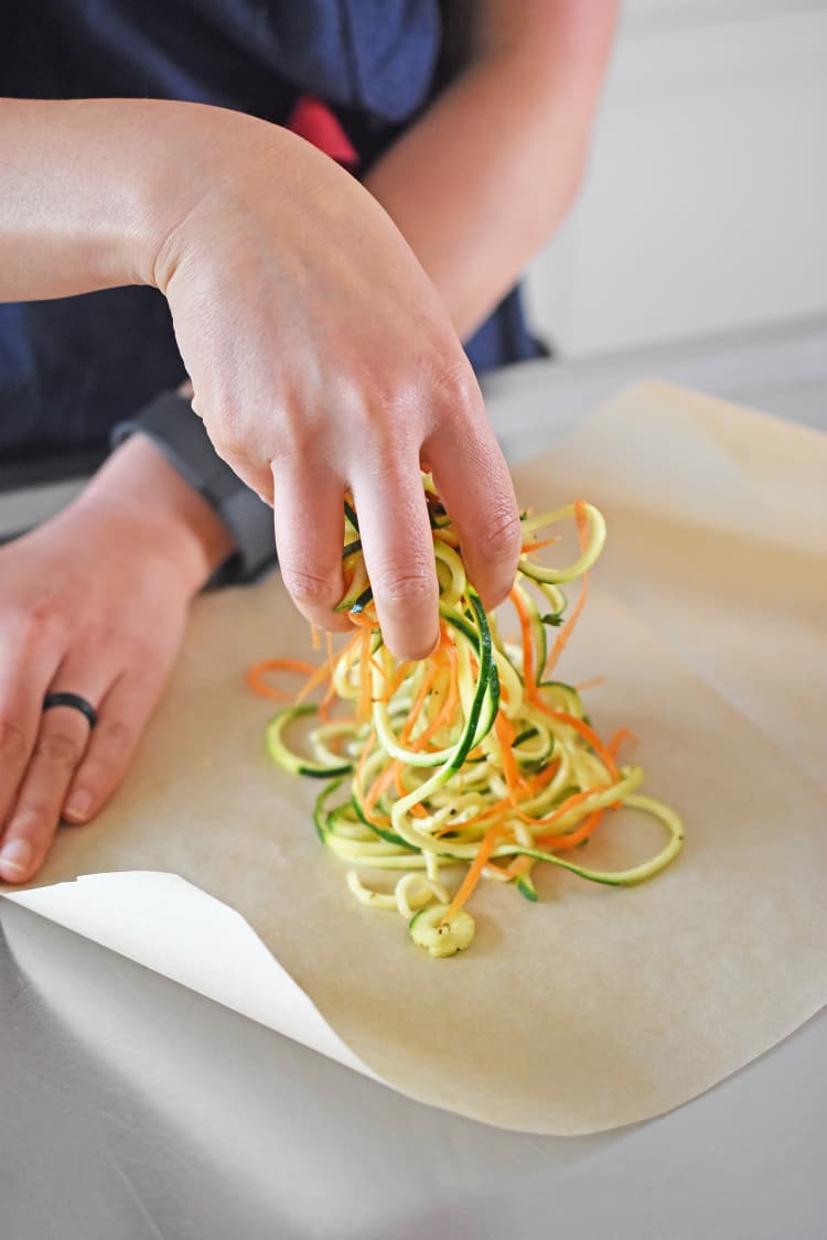 Adding seasoned spiraled vegetables to the parchment paper.