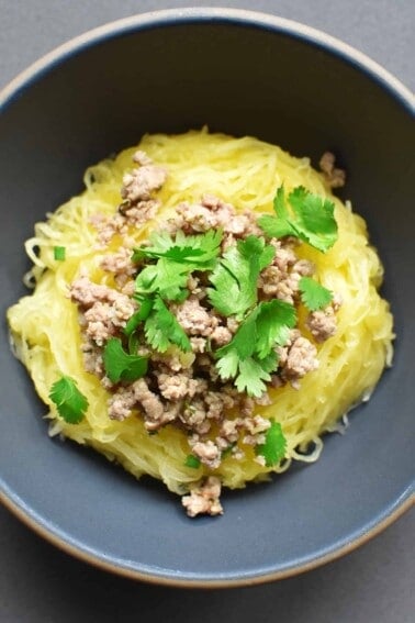 An overhead shot of a bowl of Instant Pot spaghetti squash topped with stir-fried ground pork and cilantro leaves.