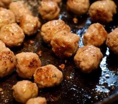 Paleo meatballs being pan fried in a cast iron skillet.