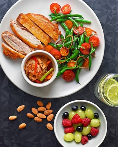 An overhead shot of a plate with crispy chicken thighs, a green bean and cherry tomato salad, and kimchi.