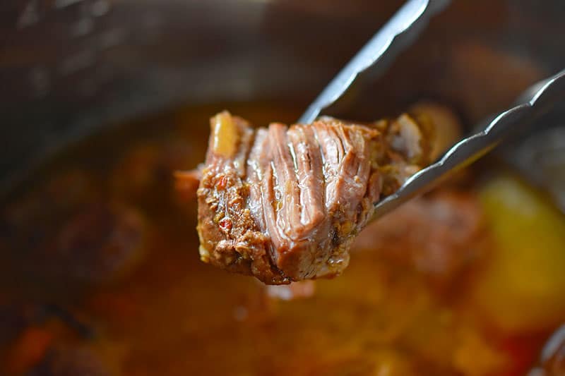 A pair of tongs holding a cooked cube of Instant Pot (Pressure Cooker) Carnitas 