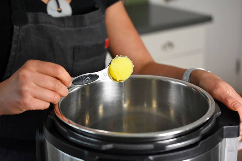 Someone adding a tablespoon of ghee to an open Instant Pot 