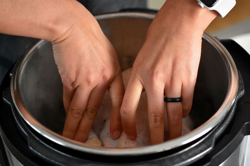 Two hands pressing a chicken breast side down in an open Instant Pot.
