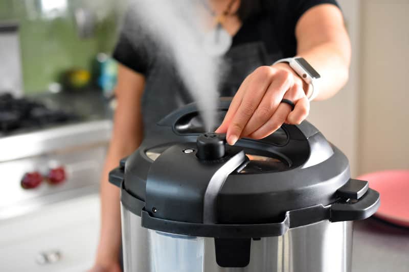 Someone turning the manual release valve on the Instant Pot and releasing steam.