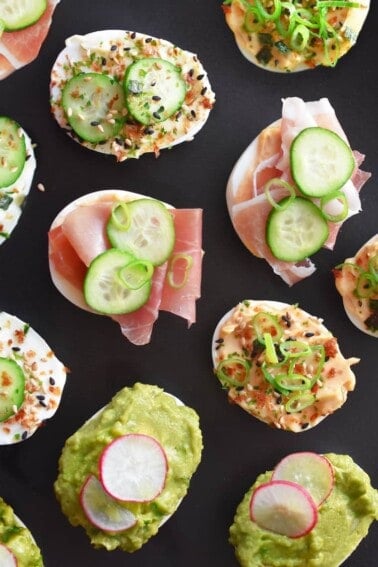 An assortment of halved hard boiled eggs from the Instant Pot topped with different toppings, like guacamole or prosciutto.