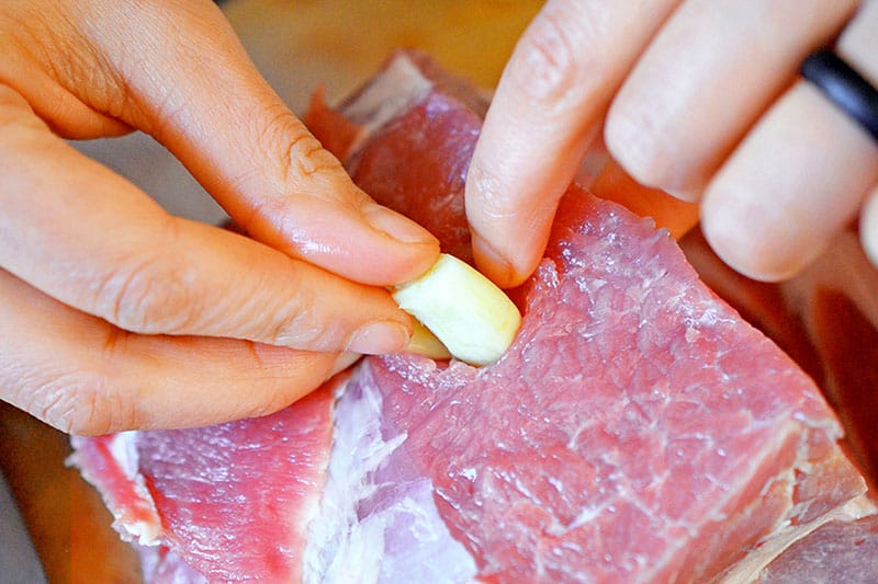 Tucking peeled garlic cloves into slits in the pork shoulder roast. 