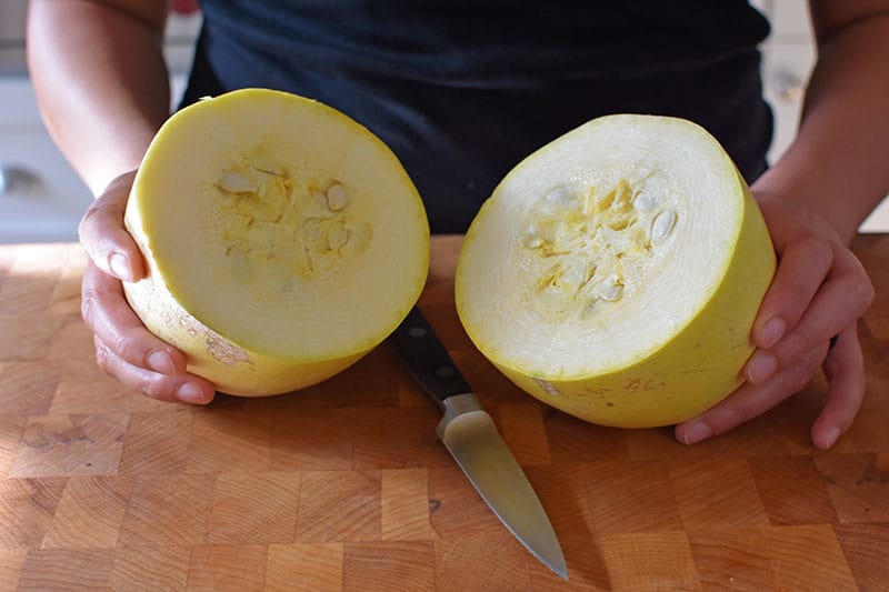 A spaghetti squash is cut in half horizontally with a small paring knife.
