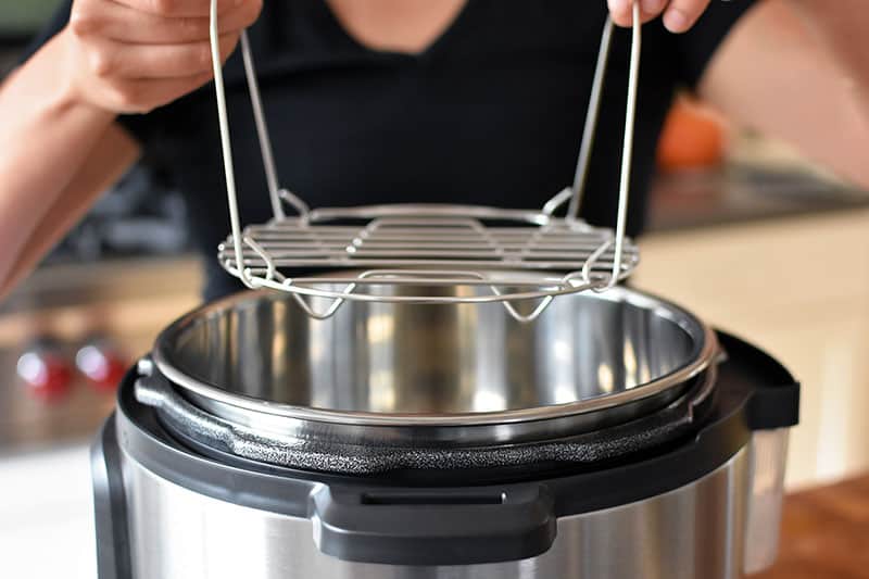 A closeup of two hands lowering a stainless steel steaming rack into an open Instant Pot.