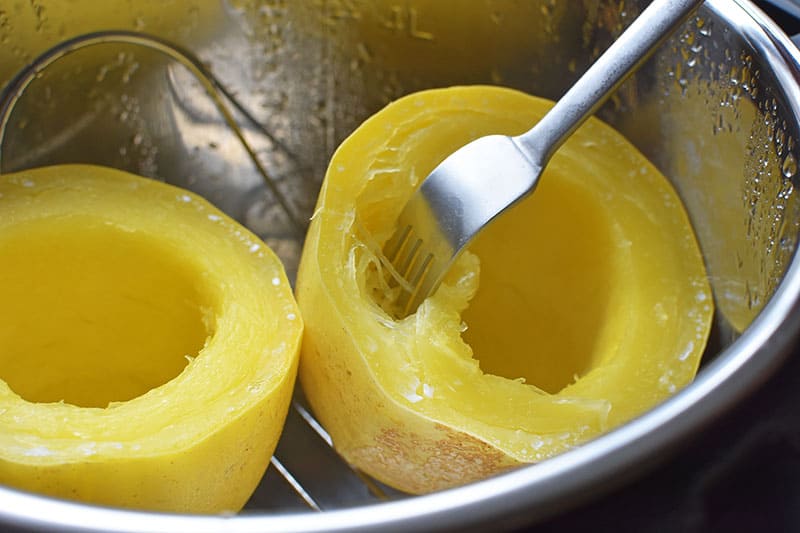 Close up of an open Instant Pot after the spaghetti squash is cooked. There is a fork poking in the spaghetti squash half on the right and the bright yellow squash flesh is shredded like noodles.