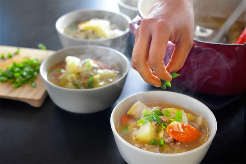Someone decorating steamy bowls of Pork and Napa Cabbage Soup