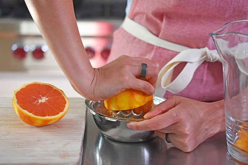 A person in a red apron is juicing a half of anorange with a manual juicer.