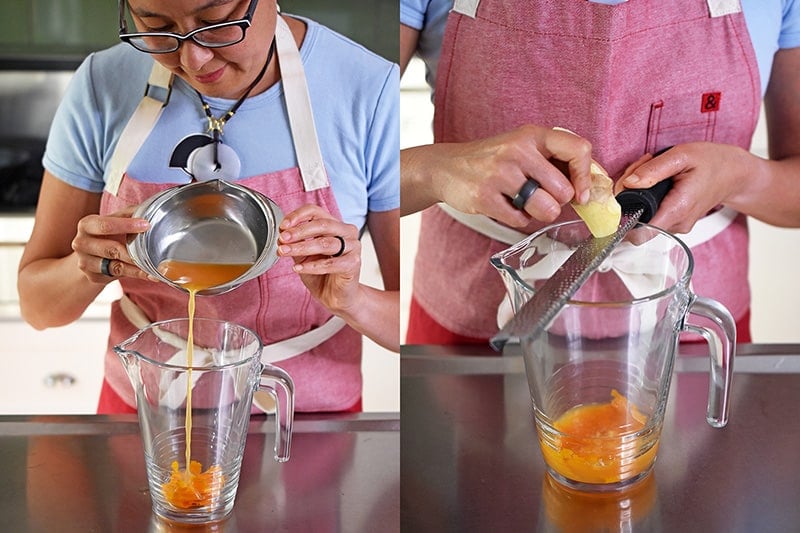 An Asian woman in glasses is pouring fresh squeezed orange juice and freshly grated ginger into a pitcher.