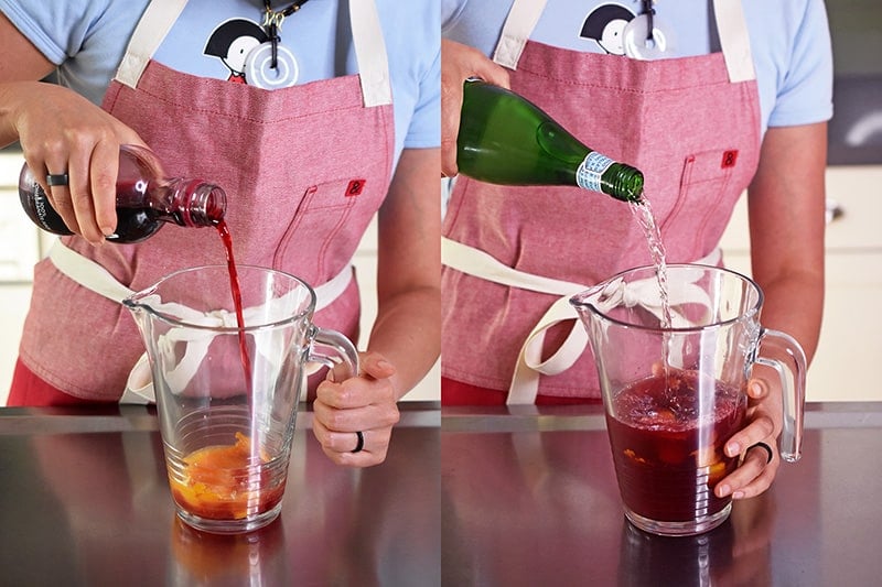A person in a red apron is pouring pomegranate juice and sparkling water into a pitcher.