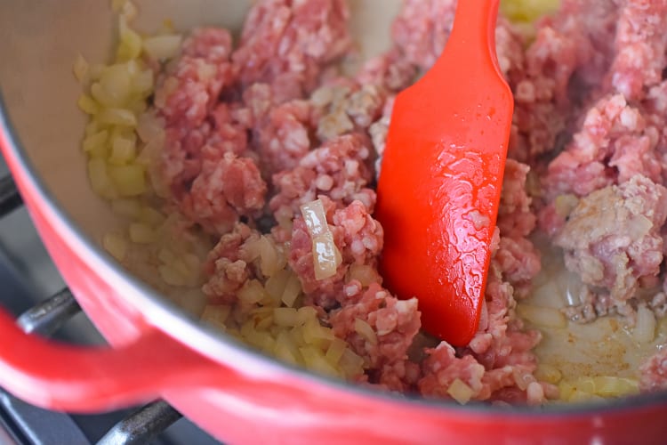 Adding ground pork to the diced onions in the stockpot