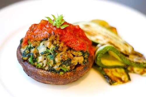 A sausage and spinach stuffed portobello mushroom topped with marinara sauce with a side of roasted zucchini.