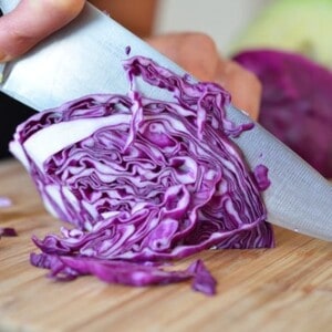 Someone slicing a red cabbage on a cutting board for paleo sautéed red cabbage with onions, garlic, and anchovy.